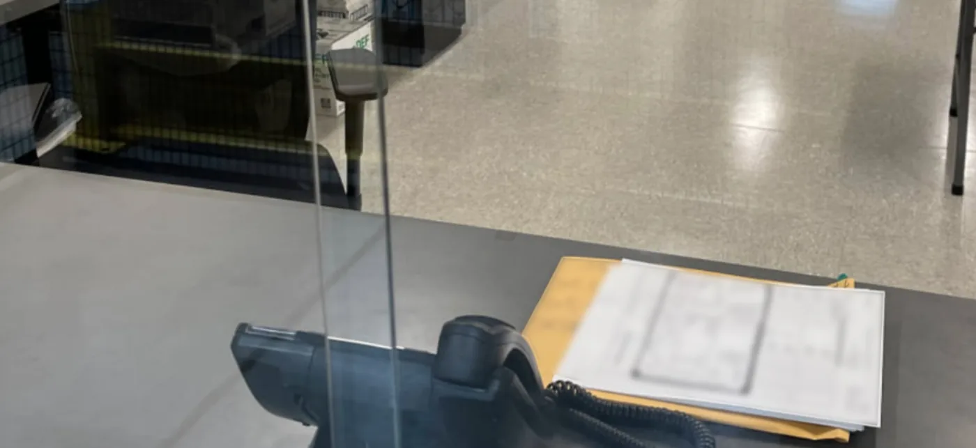 A desk phone and a stack of shipping paperwork on a reception counter, seen through a glass partition.