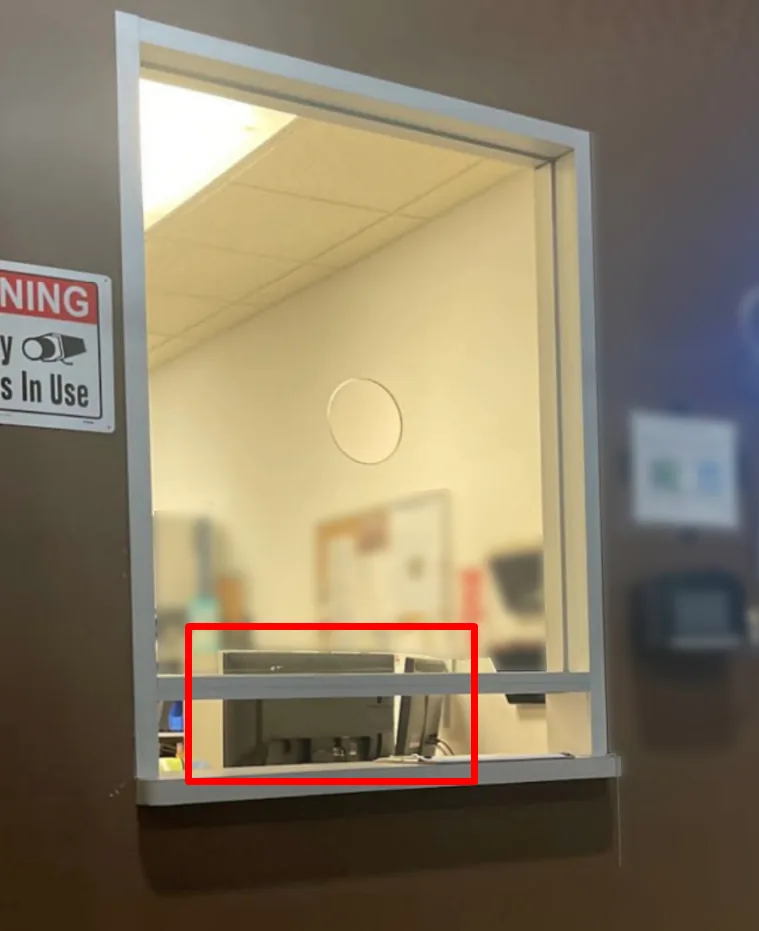 A visitor window at a logistics facility. The back of the reception monitor, with its ports, faces the window just above the document slot.